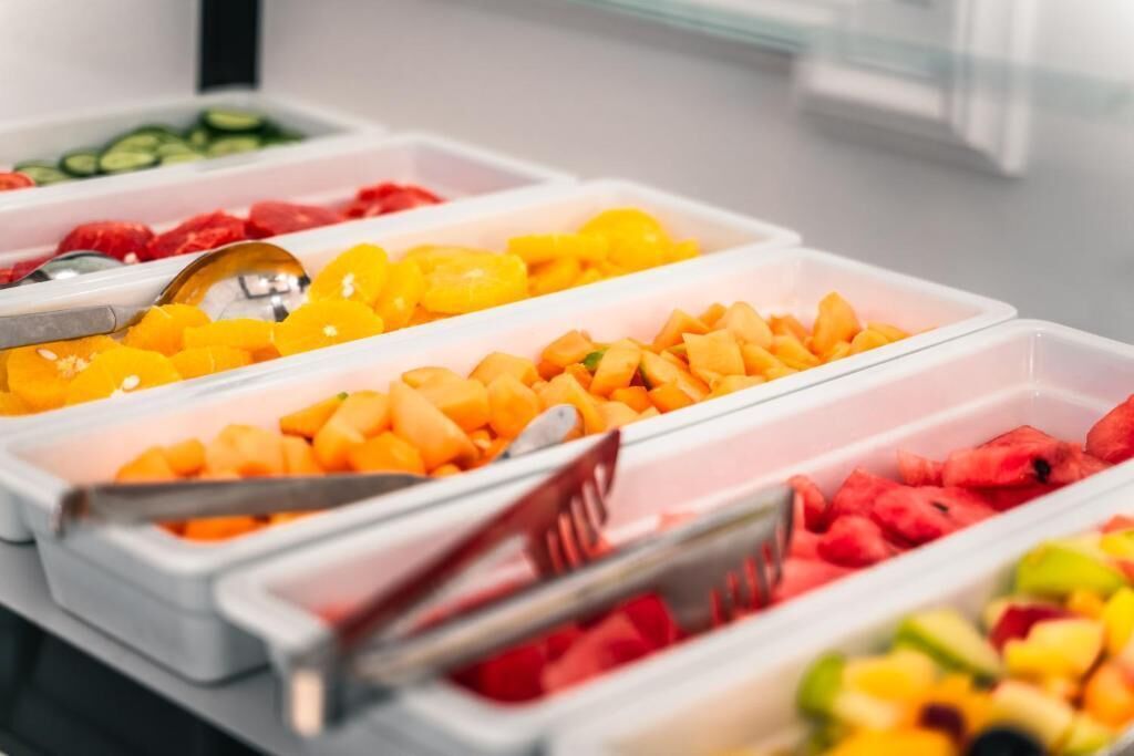 A buffet with various fruits and vegetables in clear containers.
