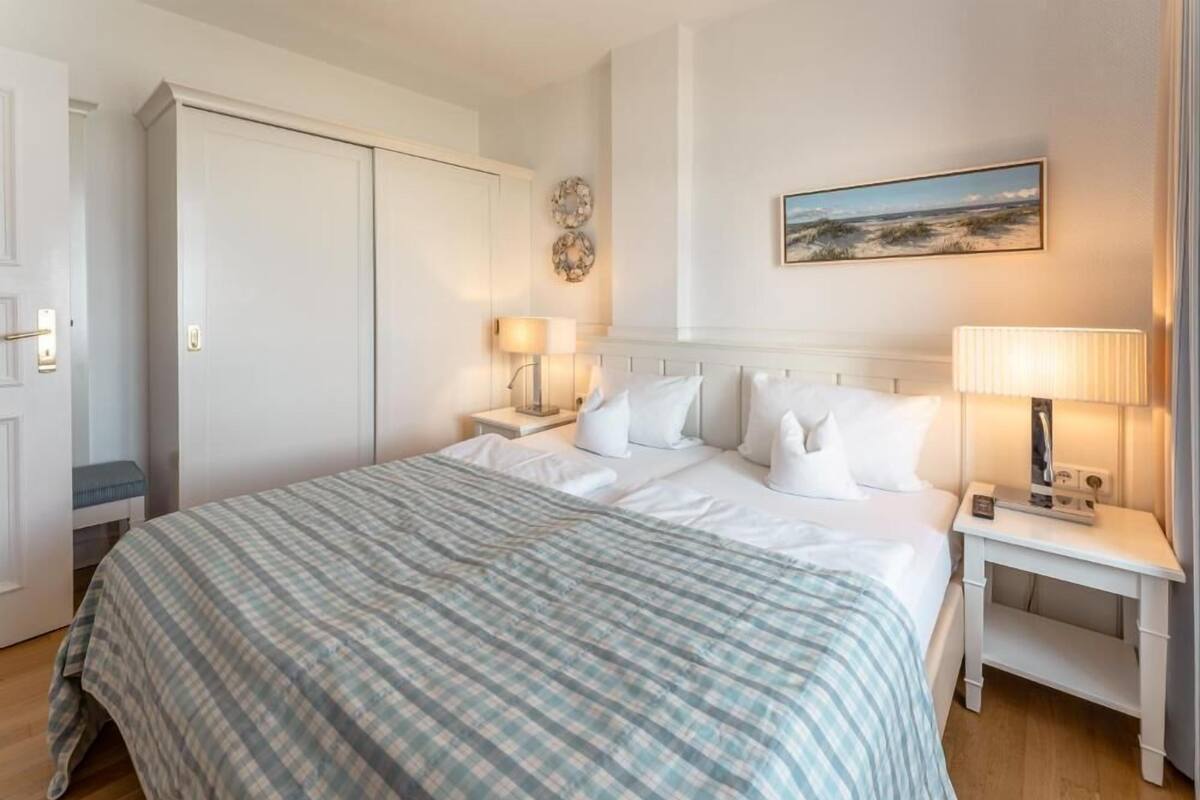 Habitación de hotel ordenada con una cama grande, una mesita de noche con lámpara, un armario y un cuadro en la pared.