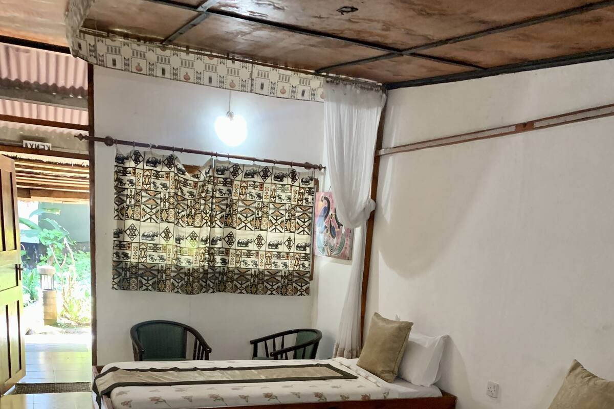 Una habitación con dos camas de madera, una silla verde y un tapiz decorativo en la pared.
