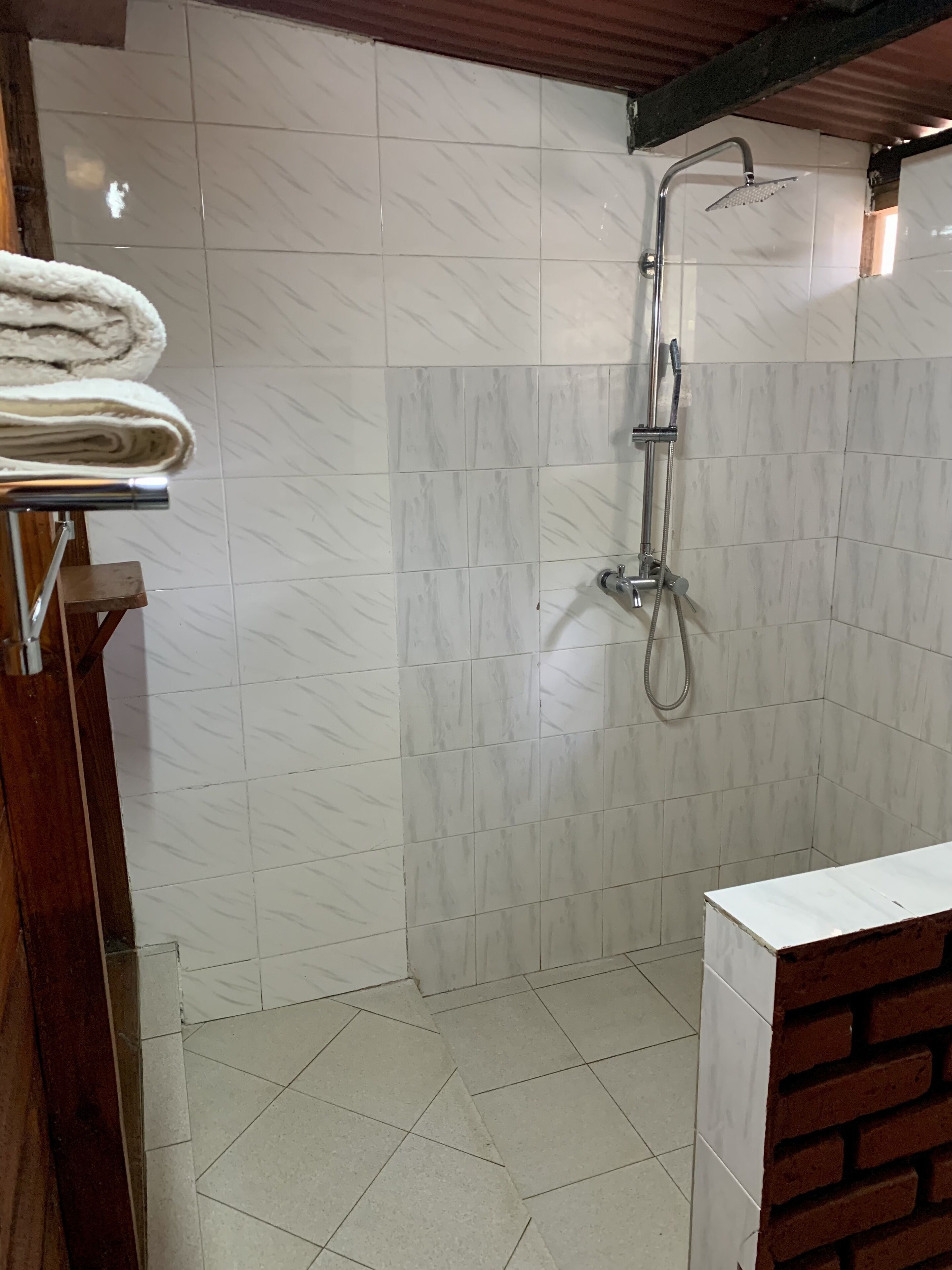 Un baño con ducha, paredes de azulejos y un banco de madera.