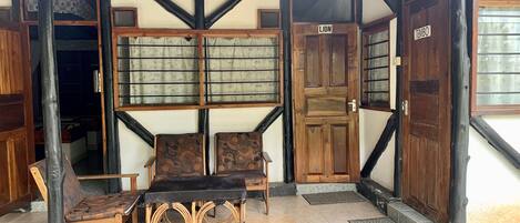 A traditional wooden building with a covered porch, two wooden doors labeled "LION" and "TEMBO," and a seating area with a table and chairs.