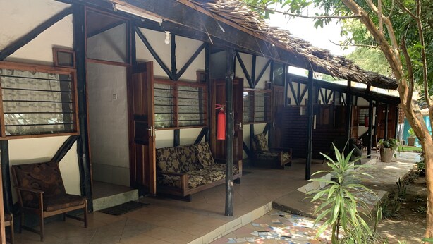 A covered outdoor seating area with wooden furniture and a tiled floor. - NEW PAMOJA RESORT (Arusha)