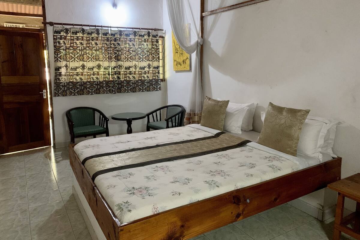 Un dormitorio con una cama de madera, dos sillas, una mesita y un tapiz decorativo en la pared.