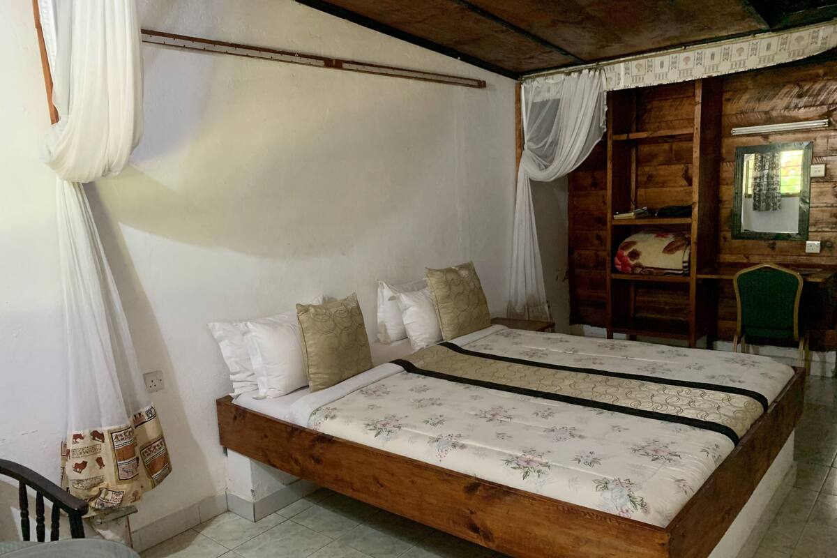 Un dormitorio con cama de madera, ropa de cama blanca, una mesita de noche, una silla y un armario de madera.