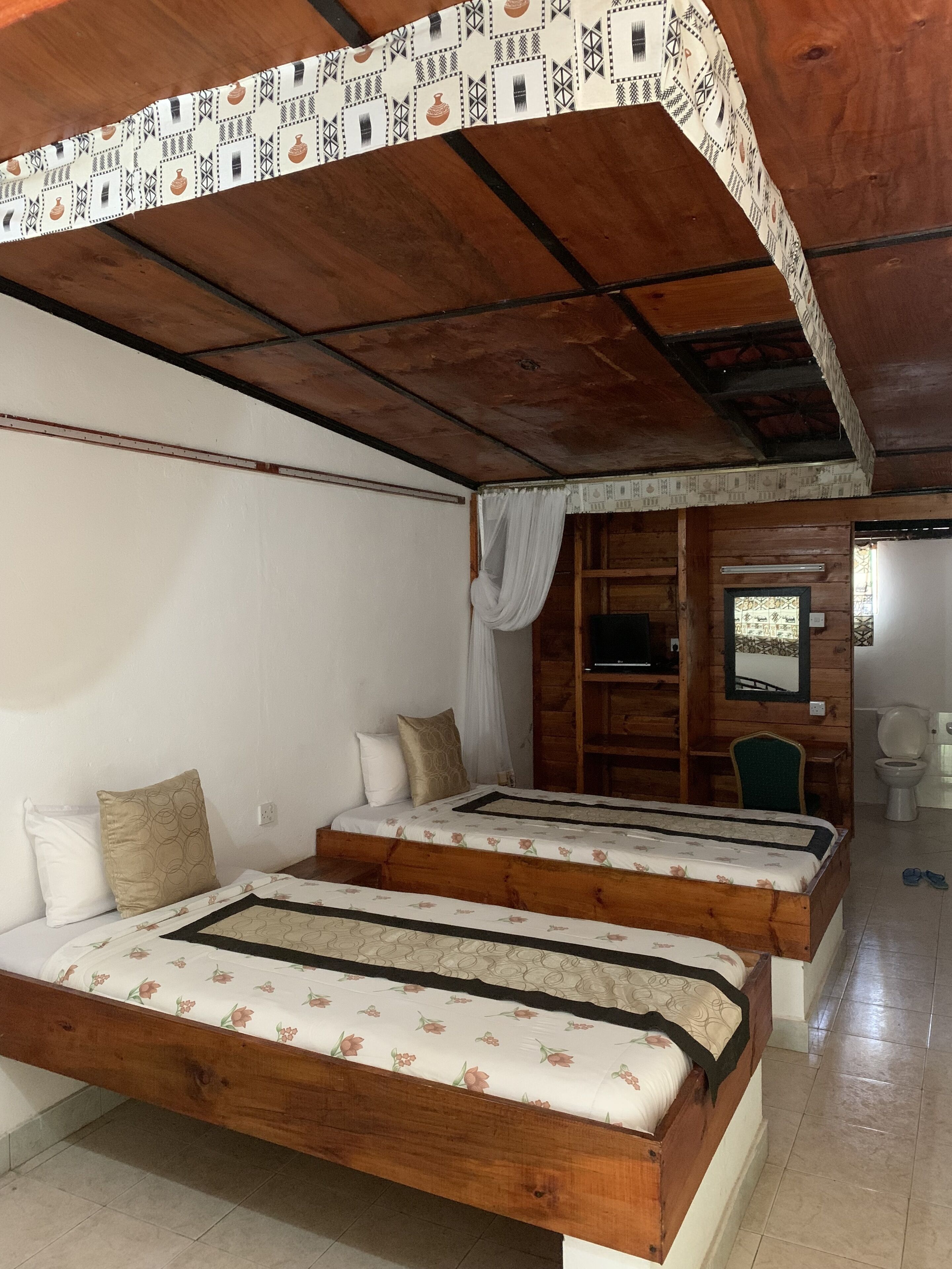 A room with two wooden beds, a small desk, and a mirror.