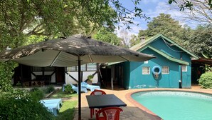 A pool area with a blue house, outdoor seating, and a covered table. - NEW PAMOJA RESORT (Arusha)