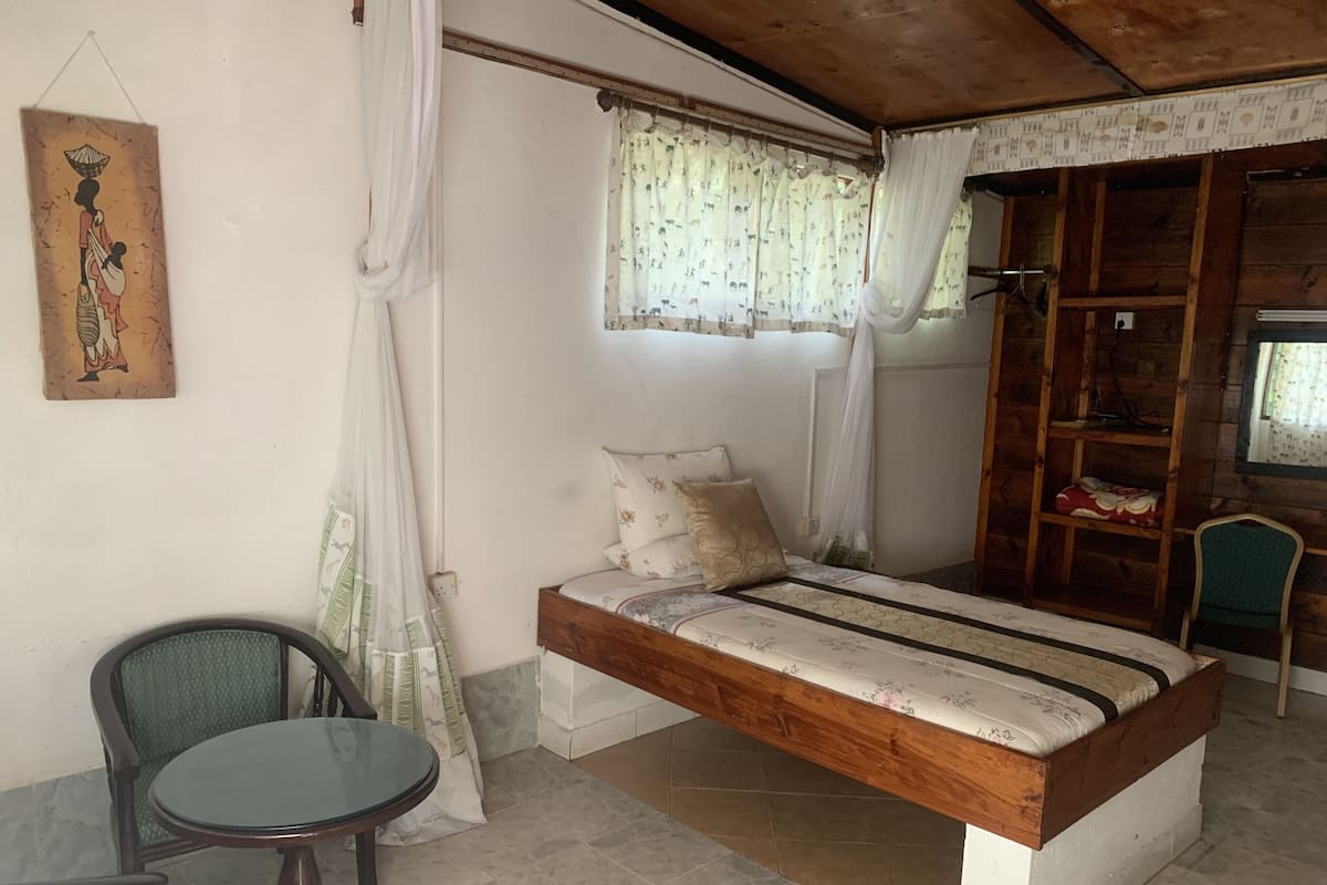 Un dormitorio con cama, una silla, una mesa y una ventana con cortinas.