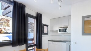 A compact kitchen with white cabinets, a microwave, and a dining area with a wooden table and chairs. - Comfy studio, ski-in/ski-out, balcony, Wi-Fi (Belle Plagne)