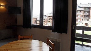 A room with a round wooden table, two chairs, a flat-screen TV mounted on the wall, and a window with black curtains. - Comfy studio, ski-in/ski-out, balcony, Wi-Fi (Belle Plagne)
