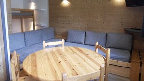 A cozy room with a wooden wall, a round wooden table, and a blue sofa. - Comfy studio, ski-in/ski-out, balcony, Wi-Fi (Belle Plagne)