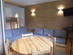 A cozy room with a wooden wall, a round wooden table, and a blue sofa. - Comfy studio, ski-in/ski-out, balcony, Wi-Fi (Belle Plagne)