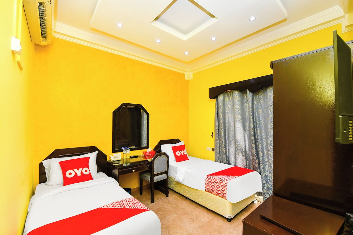 A hotel room with two beds, a desk, a chair, a television, and a mirror.