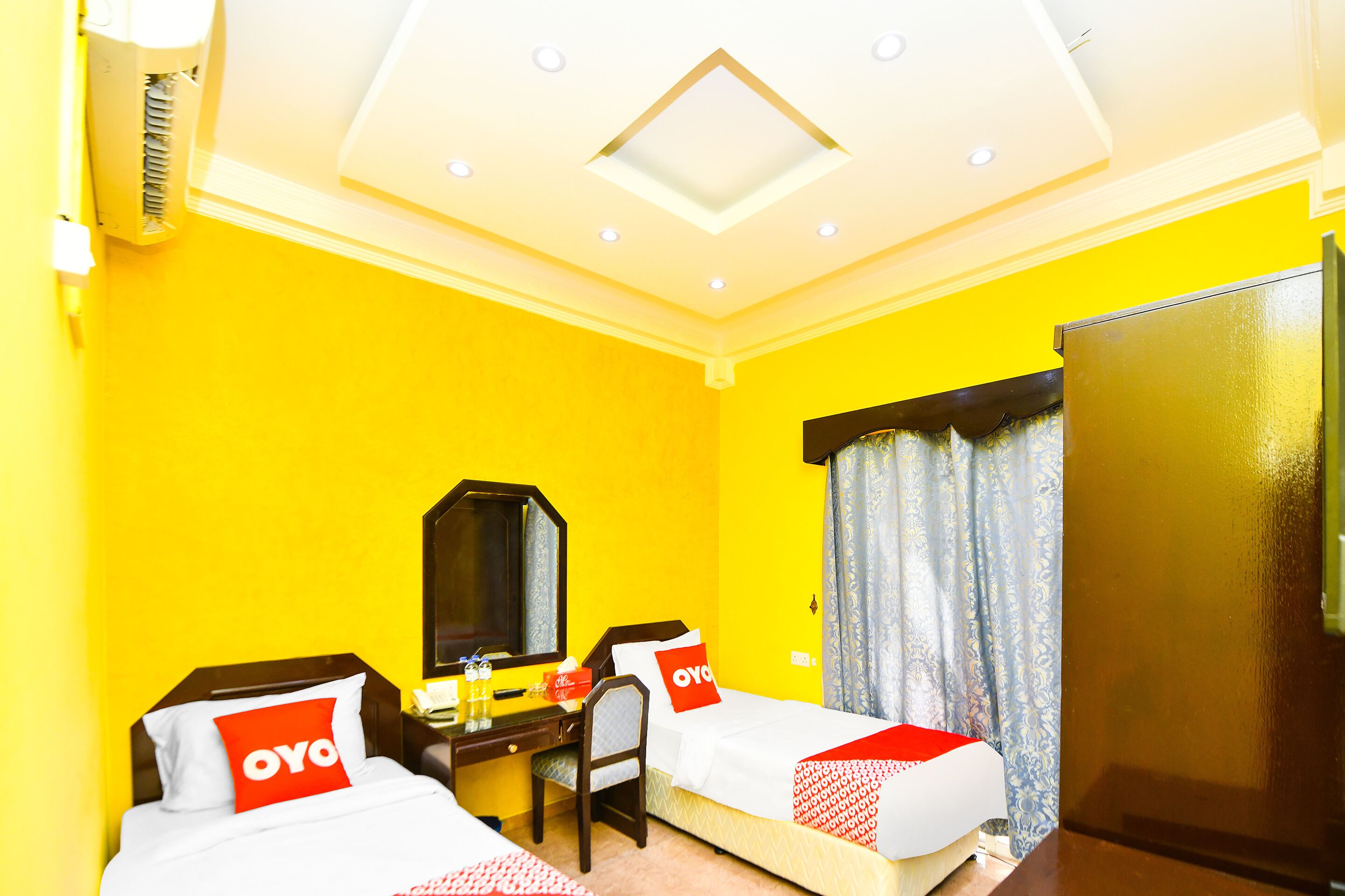 A hotel room with two beds, a desk, a mirror, and a wardrobe.