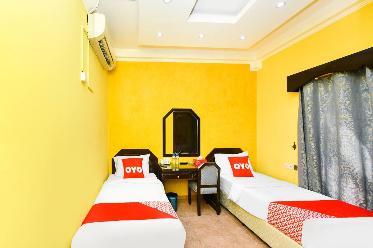 A hotel room with two beds, a desk, a chair, a mirror, and a window with curtains.