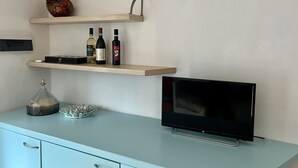 Un soggiorno moderno con una TV a schermo piatto, mobili azzurri e elementi decorativi, tra cui una statuina di cigno e bottiglie di vino.