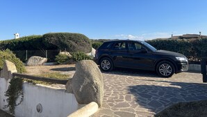 Un SUV nero parcheggiato su una superficie in pietra, con un cielo azzurro limpido e un edificio bianco sullo sfondo.