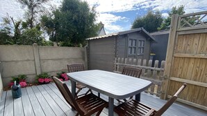 Une terrasse en bois avec une table et des chaises, entourée d’une clôture en bois et d’une maison.