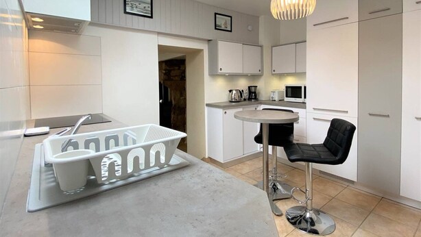 Une cuisine moderne avec des meubles blancs, une table de salle à manger ronde, un tabouret de bar et un luminaire suspendu.