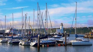 A marina with multiple boats docked, a lighthouse in the background, and a clear sky. - Boutique Fisherman's Grade II Listed Cottage (Scarborough)