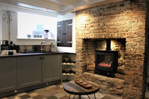 A kitchen with a stone fireplace, wooden cabinets, and a window with kitchen items on the sill.