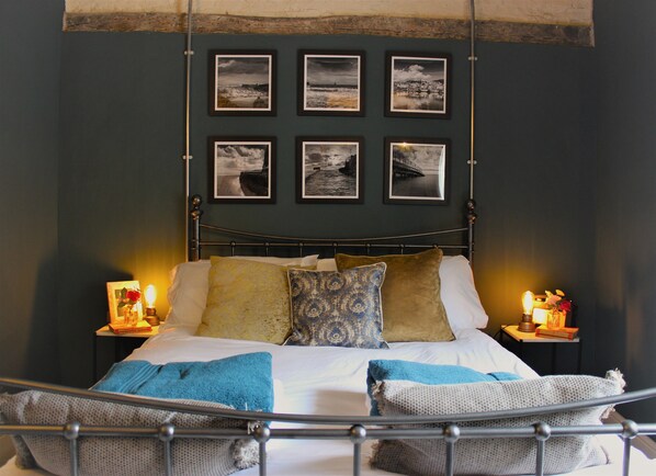 A bedroom with a metal bed frame, a dark wall, and six framed photographs above the bed. - Boutique Fisherman's Grade II Listed Cottage (Scarborough)