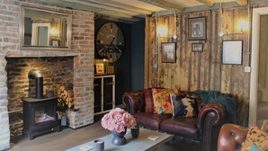 A rustic living room with a stone fireplace, leather sofa, and a large wall clock. - Boutique Fisherman's Grade II Listed Cottage (Scarborough)