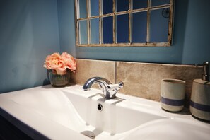 A bathroom sink with a chrome faucet, a vase with flowers, and two ceramic containers. - Boutique Fisherman's Grade II Listed Cottage (Scarborough)