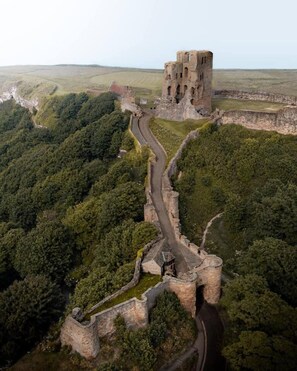 An aerial view of a historic castle surrounded by dense forest, featuring a winding path and a prominent tower. - Boutique Fisherman's Grade II Listed Cottage (Scarborough)