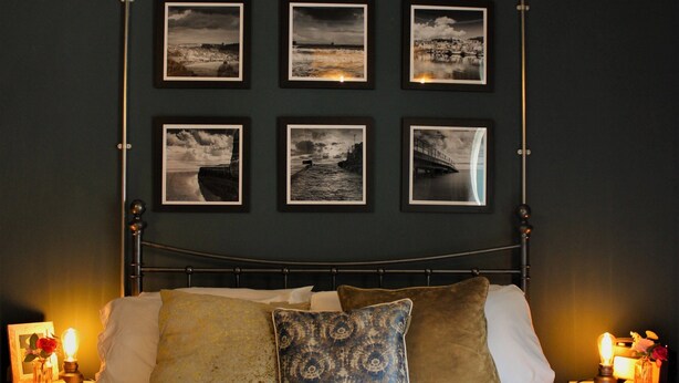 A bedroom with a metal bed frame, a white bedspread, and multiple pillows. There are framed pictures on the wall above the bed. - Boutique Fisherman's Grade II Listed Cottage (Scarborough)