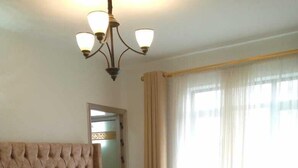 A bedroom with a tufted headboard, a large bed with white linens, a rolled towel, and a chandelier. - Stay.Plus Sandalwood Apartment Kilimani (Nairobi)