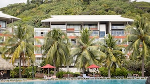 Un hôtel doté d’une piscine, entouré de palmiers et bordé d’une colline verdoyante.