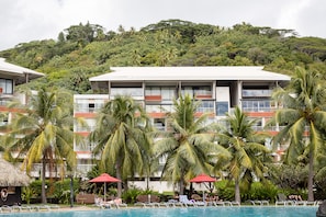 Un hôtel doté d’une piscine, entouré de palmiers et bordé d’une colline verdoyante.