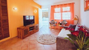 Ein Wohnzimmer mit Fernseher, zwei Sesseln, einer Couch und einer Pflanze.