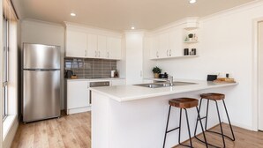 Cocina moderna con armarios blancos, refrigerador de acero inoxidable, salpicadero de azulejos y una zona de bar con taburetes.