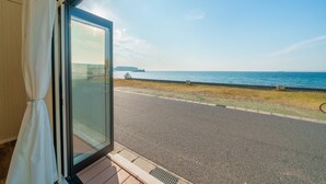 A view from a room with a large window overlooking a coastal road with a grassy area and a metal fence. - Ryushima Ocean View Villa (Kyonan)