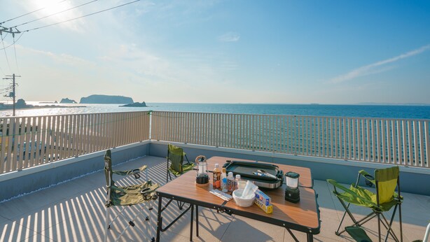 A balcony with a table set for dining, overlooking a body of water and distant land. - Ryushima Ocean View Villa (Kyonan)
