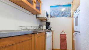 A compact kitchen with wooden cabinets, a dishwasher, a coffee maker, and a hanging laundry bag. - Functional apartment in the center with balcony in La Plagne (La Plagne Montchavin Les Coches)
