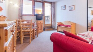 A cozy room with a wooden dresser, a red sofa, a wooden chair, a television, and a window with curtains. - Functional apartment in the center with balcony in La Plagne (La Plagne Montchavin Les Coches)