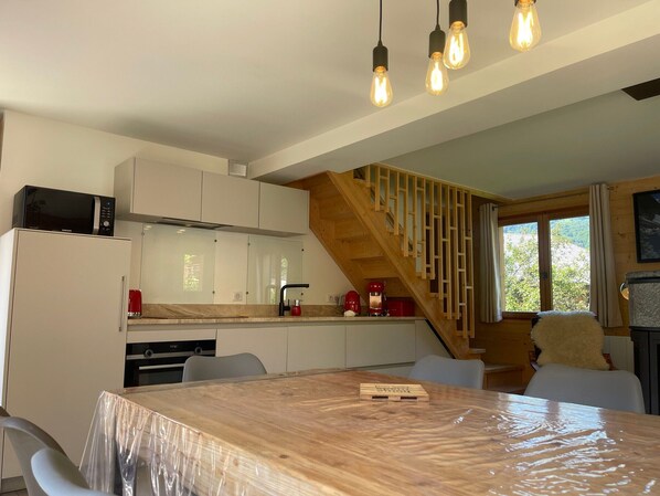 Una cocina moderna con armarios blancos, una escalera de madera y una mesa de comedor con sillas.