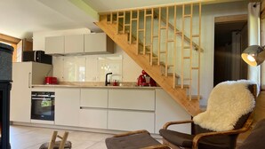 A modern kitchen with white cabinets, a wooden staircase, and a cozy seating area with a fluffy chair and ottoman. - Spacious chalet near shops, pets allowed! (Samoëns)