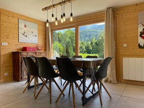 Un comedor con una mesa y sillas de madera, una ventana con vista a la vegetación y una lámpara en el techo.