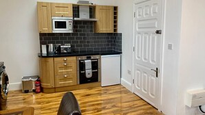 A compact kitchen with wooden cabinets, a microwave, a toaster, and a small oven. - Charming 1-bed Apartment in Lytham Saint Annes (Lytham St. Anne's)