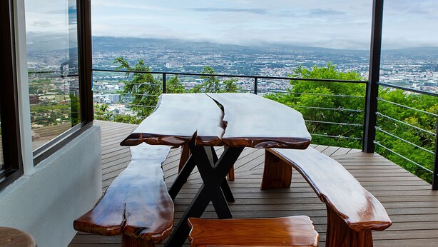 A wooden deck with a picnic table and benches, overlooking a cityscape. - Cozy Loft with big terras having a spectaculair view of San Jose (San Antonio de Escazú)