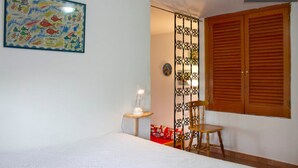 Une chambre à coucher comprenant un lit, une chaise, une table de chevet, un panneau décoratif et une porte en bois.