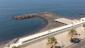 Une vue sur la côte, avec une digue rocheuse, une promenade et un bâtiment doté d’un toit plat.
