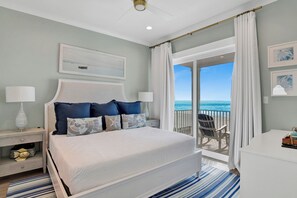 A bedroom with a large bed, a nightstand, a desk, and a view of the ocean. - Beachfront Luxury | Heated Pool | Elevator | EV Charger (Gulf Shores)
