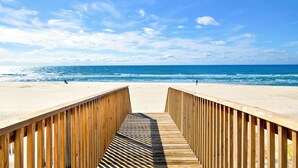Un muelle de madera que lleva a una playa arenosa con el océano al fondo.