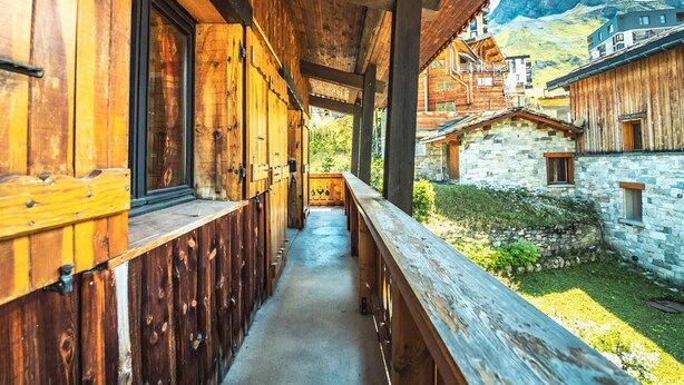 Ein hölzerner Korridor mit Balkon, der zu einem Steinhaus mit Bergblick führt.