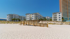 Un hotel frente a la playa con varias edificaciones blancas, un muelle de madera y una playa de arena.