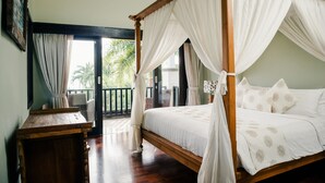 A four-poster bed with white bedding and a wooden frame, a wooden nightstand, and a view of the outdoors through a glass door. - Sunset Villa by Premier Hospitality Asia (Nusa Dua)